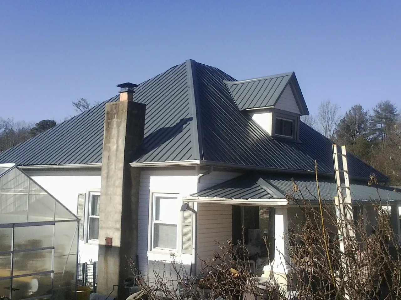 Dark blue standing seam metal roof on a white farmhouse with dormer — Slate & Tile Roof Repair by Roofing Brothers in Pattersonville