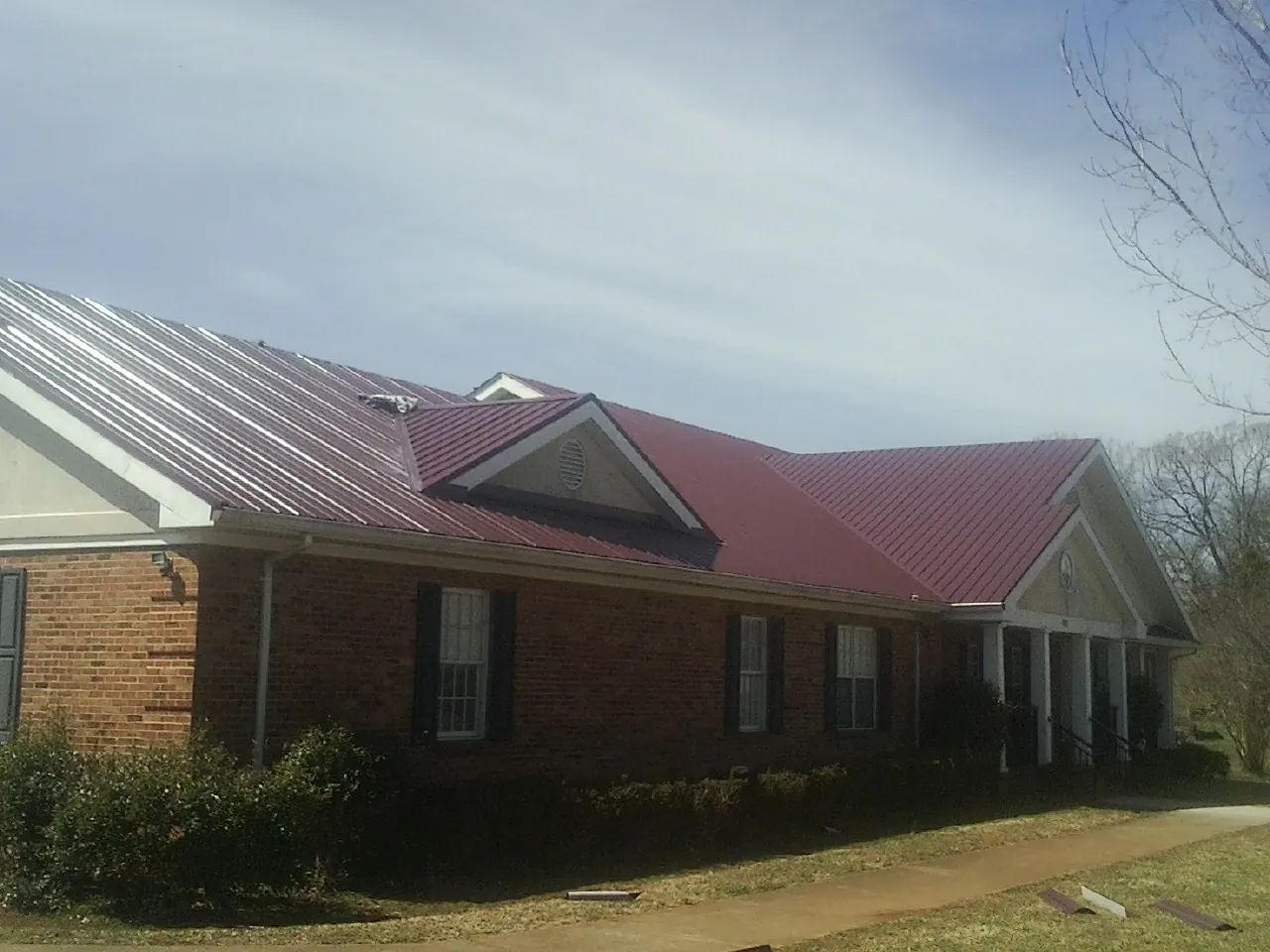 Red metal roof with gabled entries on a long brick building, from a Hail Damage Roof Repair job in Pattersonville