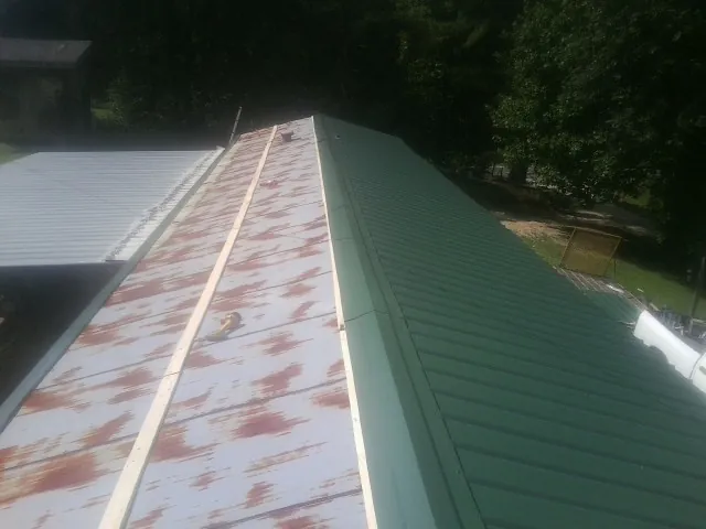 Old rusted panels beside newly installed green metal roofing — Wind Damage Roof Repair by Roofing Brothers in Pattersonville