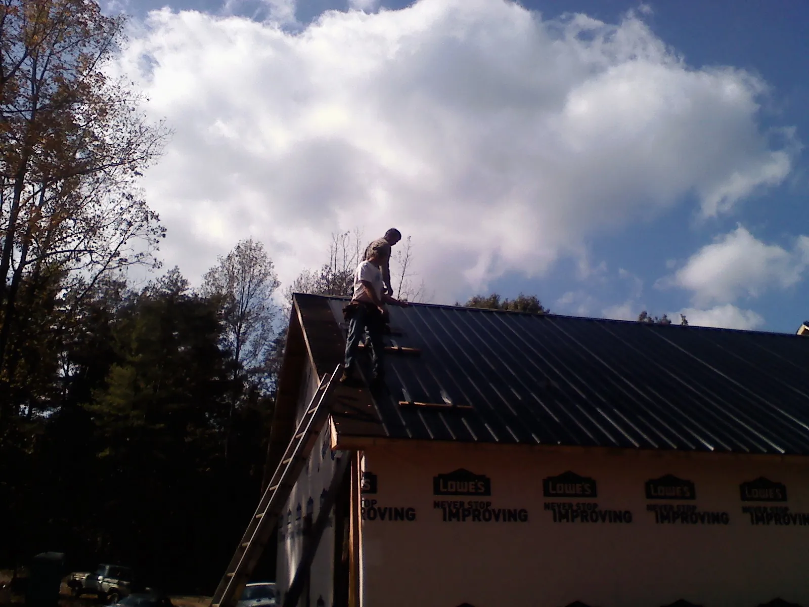 Roofer fastening dark metal panels high against a cloudy sky, from a Roof Inspection job in Pattersonville