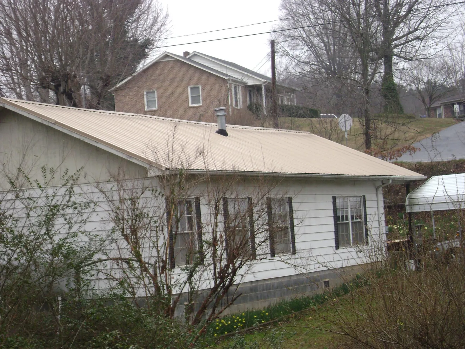 Tan metal roof on a white sided house set into a hillside — Commercial Roofing by Roofing Brothers in Pattersonville